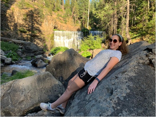Emily Judith Mitnick leans on the rock with waterfall in background